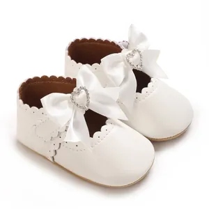 Nahaufnahme weißer Baby-Prinzessin-Schuhe mit Satinschleife und Herz-Strass-Detail.