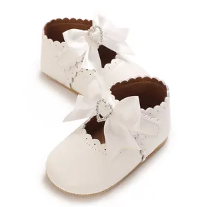 Nahaufnahme weißer Baby-Mary-Janes mit Schleife und herzförmigem Strassstein für Mädchen.