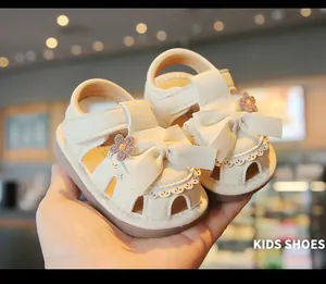 Nahaufnahme von cremefarbenen Baby-Mädchen-Sandalen mit Schleife und kleinen Blumen