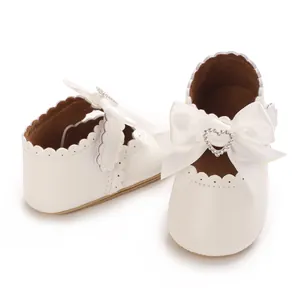 Nahaufnahme weißer Baby-Prinzessinenschuhe mit großer Satinschleife und Strass-Herzverschluss