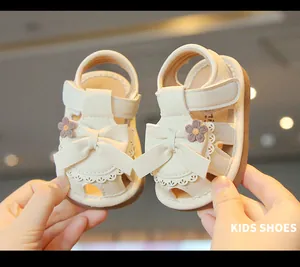 Nahaufnahme von cremefarbenen Babysandalen für Mädchen mit Schleife und Blumen.