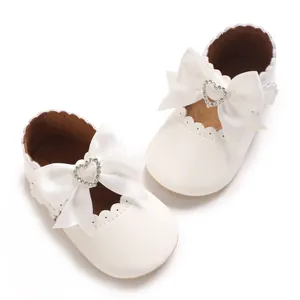 Detailansicht weißer Baby-Prinzessinnenschuhe mit großer Satinschleife und Herz-Strass