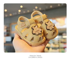 Detail view of brown baby soft-sole sandals featuring a cute bear charm and velcro strap