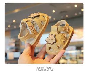 Close-up of beige soft-sole baby sandals featuring cute lucky bear and velcro strap