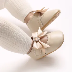 Detailansicht eleganter beiger Baby-Prinzessinenschuhe mit Satinschleife und Herz-Strass-Schnalle.