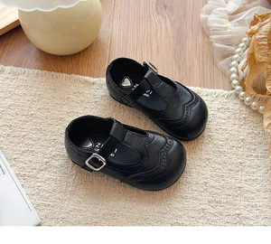 Detailed view of black leather T-strap girls' shoes with classic brogue wingtip patterns
