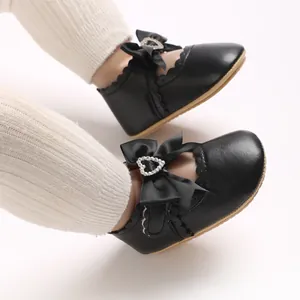 Nahaufnahme der schwarzen Baby-Mary-Janes mit Schleife und Herz-Strass-Schnalle
