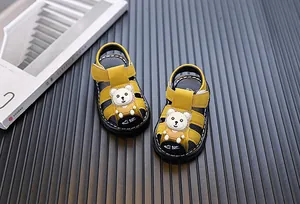 Detailed view of yellow baby sandals with cute cartoon bear on dark slatted floor
