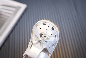 Primer plano detallado de sandalias blancas para bebé con lazo y perlas decorativas