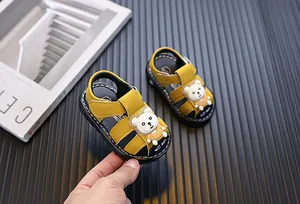 Macro view of yellow baby closed-toe sandals featuring a cute cartoon bear and velcro strap.