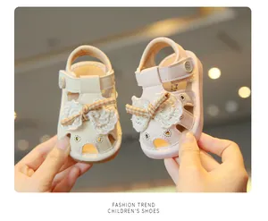 Close-up of pink and beige baby sandals with lace bow and heart cutouts.
