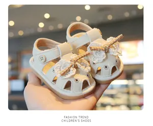 Close-up of beige baby sandals with lace bows and heart cutouts held in hand