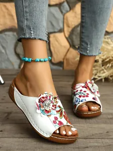 Modische Vintage-Keilsandalen mit Blumenstickerei und 3D-Blumendetail, am Modellfuß gezeigt