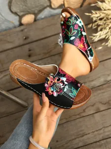 Detailansicht der schwarzen Keilsandalen mit Blumenstickerei und 3D-Blumenakzent.