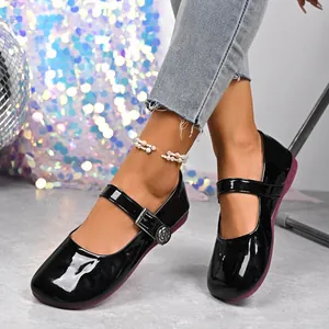 Detail of black patent leather Mary Jane flats with floral buckle accent on model