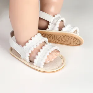 Detail showing white baby walking sandals with pom-pom trim and soft non-slip sole.
