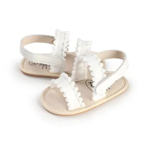 Close-up view of soft white newborn baby sandals with cute pom-pom ruffle straps