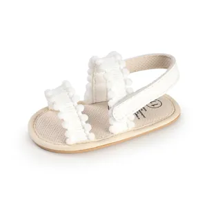 Close-up view of white infant walker sandals featuring decorative fuzzy pom-pom straps