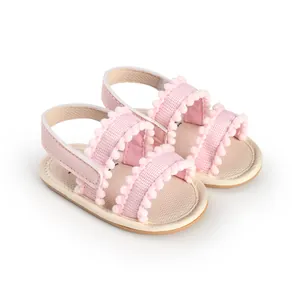Soft pink baby walking shoes featuring decorative pom-pom trim and adjustable straps