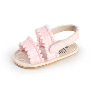 Close-up of pink baby sandal with soft pom-pom straps and adjustable velcro heel strap.