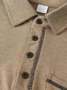 Détail macro d'un polo pour homme montrant le tissu brun, les boutons et l'étiquette.