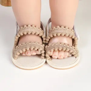 Detailed view of soft beige infant sandals featuring decorative pom-pom straps