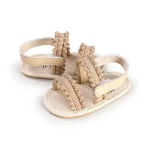 Detailed view of beige baby sandals with soft soles and decorative pom-pom straps