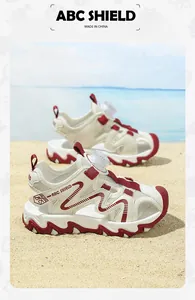 Stylish cream and red children's closed-toe beach sandals with rotary buckle closure on sand