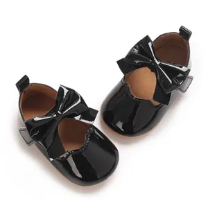 Détail de chaussures bébé en cuir verni noir avec un joli nœud et une bride velcro