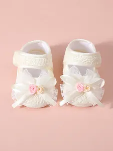 Macro view of cream lace baby princess pre-walker shoes featuring a large decorative bow