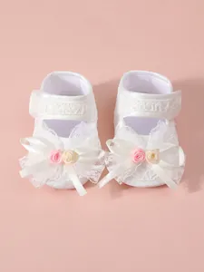 Close-up of white lace baby girl princess shoes with decorative bows and flowers
