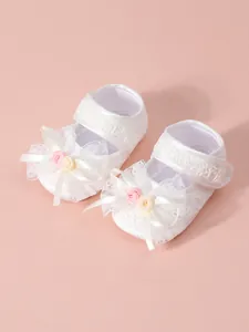 Close-up detail of elegant white lace baby princess walking shoes with a floral bow