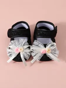 Close-up detail showing the intricate white lace bow and roses on black baby shoes