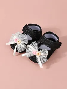 Detailed view of baby girl princess shoes with delicate white lace bows and floral accents