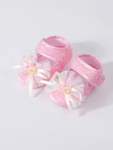 Close-up of pink lace baby princess shoes with delicate ribbon bows and small roses