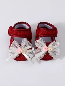Close-up of red lace baby princess shoes with elegant white bows and pink roses