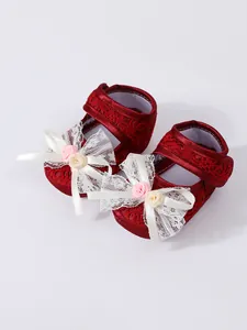 Detail of red lace baby princess shoes with delicate white bows and fabric roses.