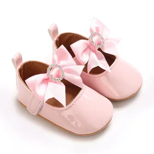 Nahaufnahme von rosa Lackleder-Babyschuhen mit großen Satinschleifen und Strasssteinen.