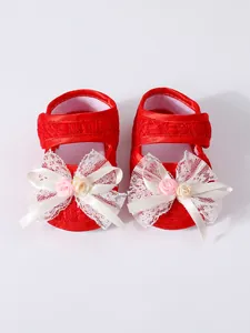 Close-up of red baby girl princess pre-walker shoes featuring a delicate white lace bow.