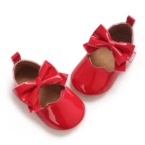 Vue détaillée de chaussures de bébé fille en cuir verni rouge avec un grand nœud décoratif.