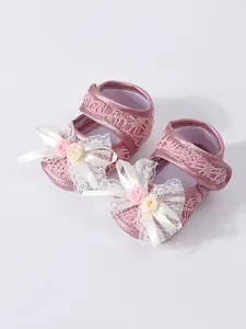 Detail view of pink lace baby princess shoes with elegant white bow and rose accents