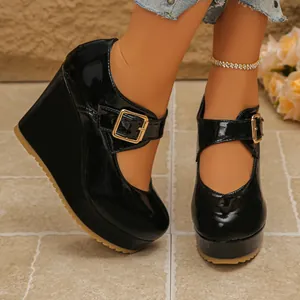 Detailed shot of black patent Mary Jane wedge shoes with square toe and gold buckle.
