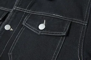 Dettaglio della tasca di una giacca di jeans nera con bottoni argentati e cuciture bianche