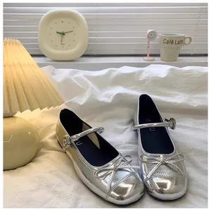Zilveren Mary Jane schoenen voor meisjes met strikje en gesp op wit beddengoed.