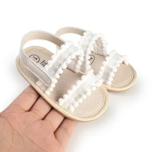 Bequeme weiße Babysandalen mit Bommelbesatz für Lauflerner im Alter von 0-1 Jahr.