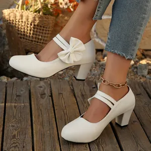 Zapatos elegantes blancos de tacón grueso con lazo y tira Mary Jane sobre suelo de madera