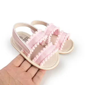 Nahaufnahme von rosa Baby-Lauflernsandalen mit Bommeln auf der Hand