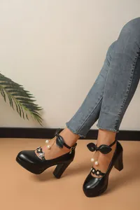 Gros plan de talons hauts noirs avec brides à nœud et breloques en perles pendantes