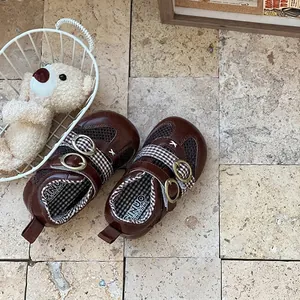 Detailed view of brown mesh toddler shoes with double buckle straps on stone floor.