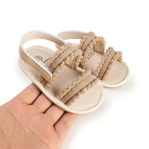 Detail von beigen Baby-Lauflernschuhen mit süßem Bommelbesatz in der Hand.